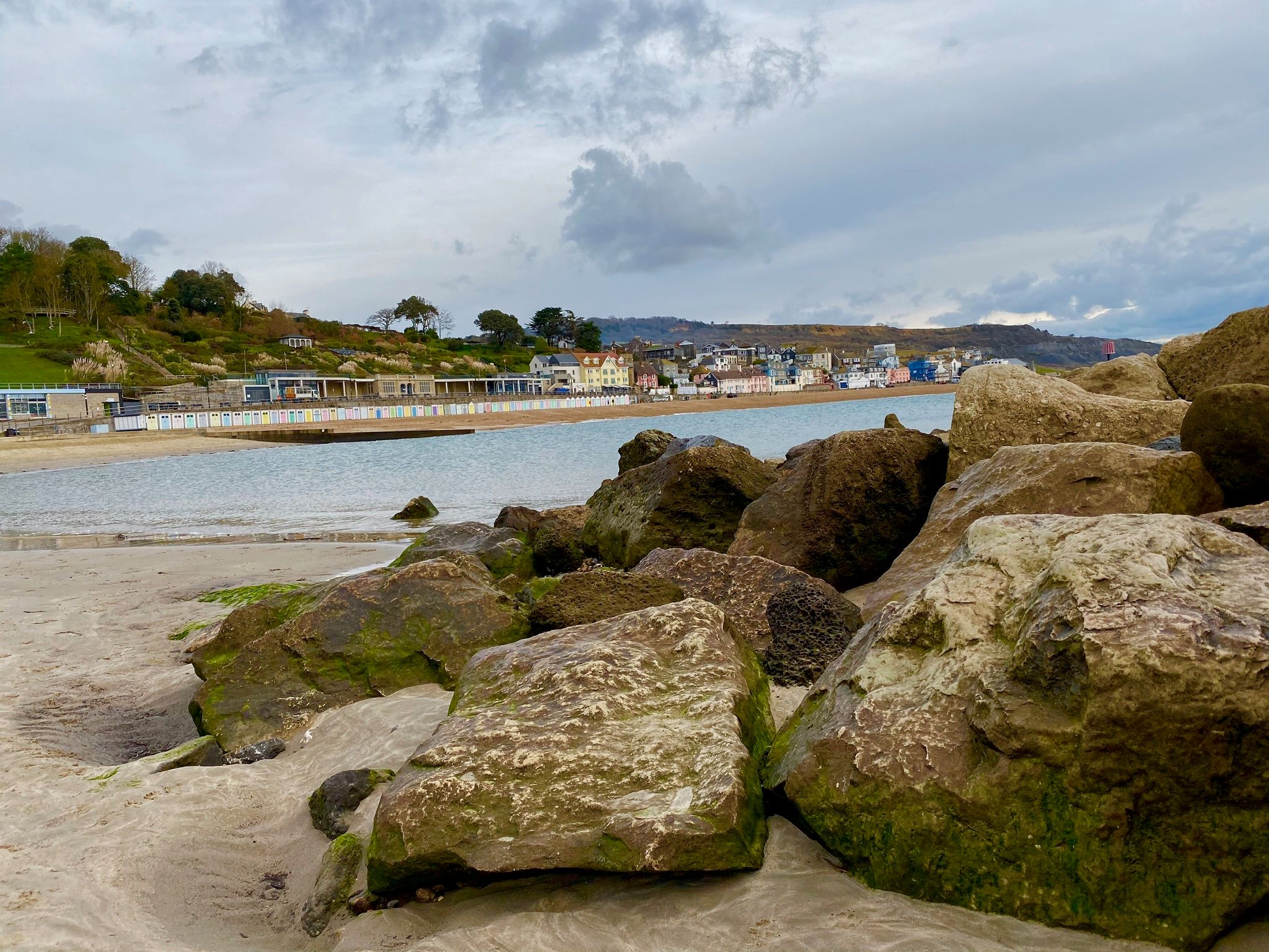 Mossy rocks on a sandy beach looking toward a town.