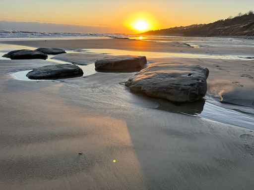 Golden sunset reflecting on a sandy beach with rocks.