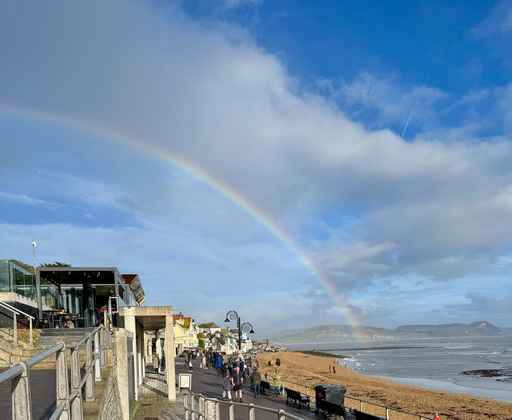 Bright rainbow stretching over a coastal promenade and beach.