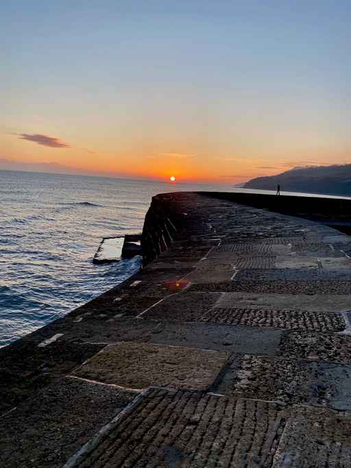 Sunset view along a stone harbour wall.