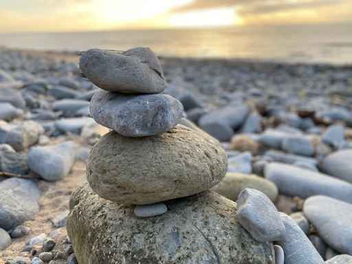 Stack of smooth stones balanced on a pebble beach at sunset.